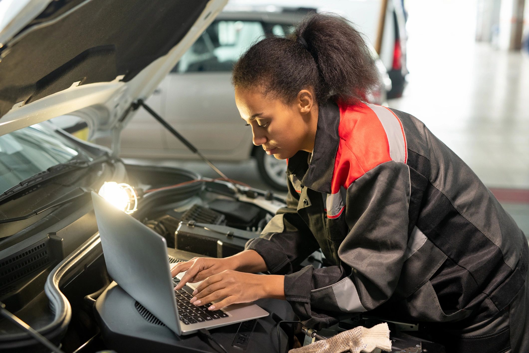 Technician using a laptop to diagnose a vehicle with the hood open