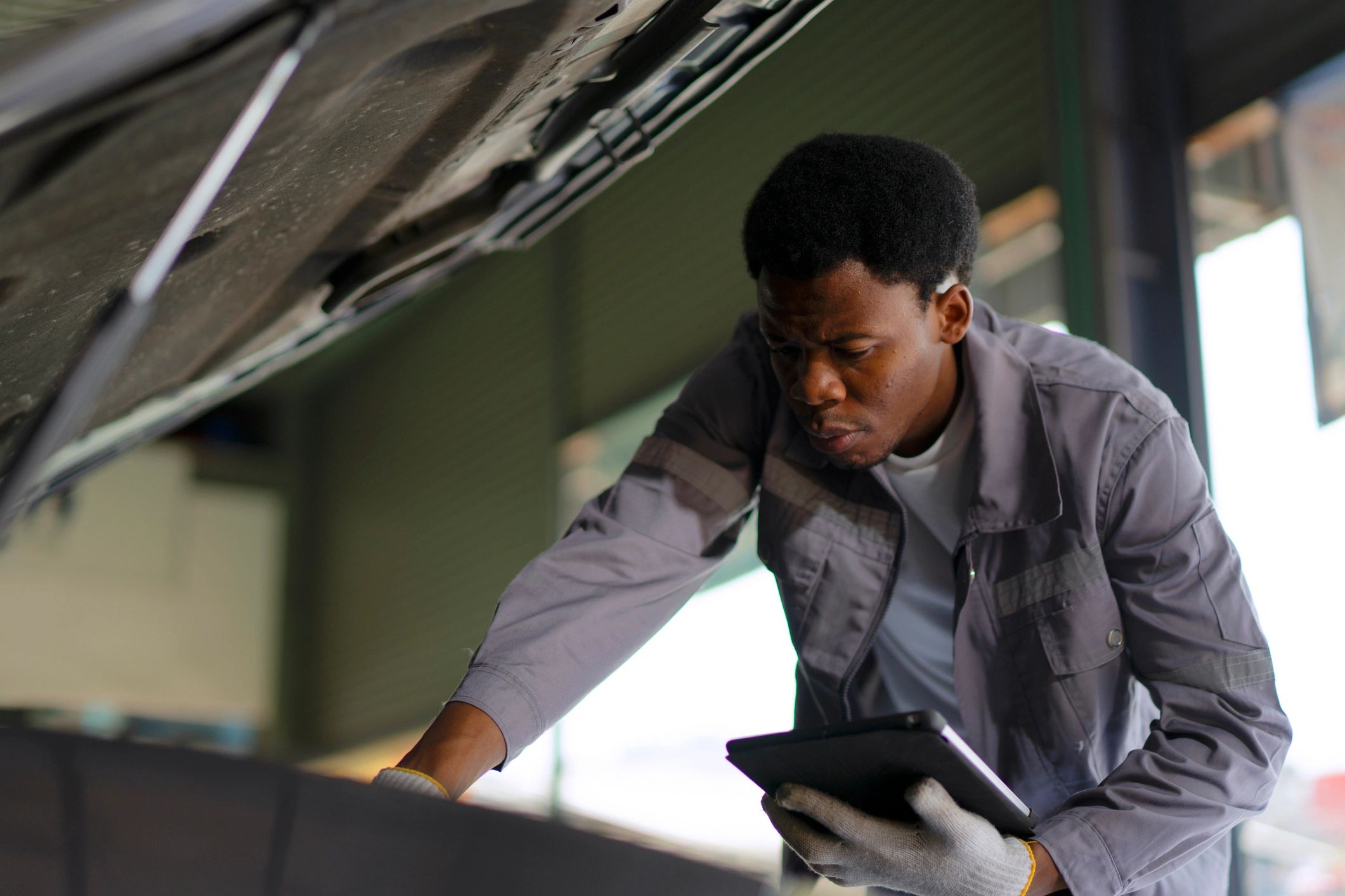 Technician inspecting a vehicle with a diagnostic tablet in a service bay